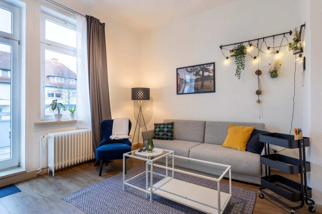 Heller Wohnraum mit grauem Sofa, blauer Sessel und Pflanzen an der Wand , Cozyhomes Ferienimmobilien, Ferienwohnung Bad Arolsen, Ferienhaus Kellerwald, Ferienhaus Edersee, Ferienwohnung Arolsen
