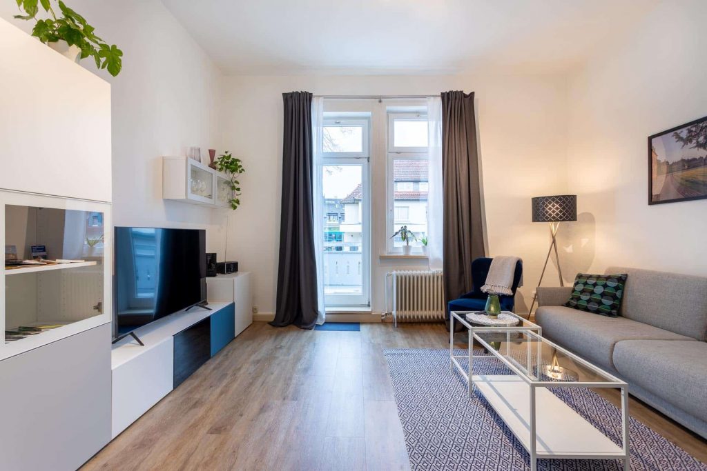 Heller Wohnraum mit Sofa, Fernseher und großem Fenster in moderner Einrichtung , Cozyhomes Ferienimmobilien, Ferienwohnung Bad Arolsen, Ferienhaus Kellerwald, Ferienhaus Edersee, Ferienwohnung Arolsen